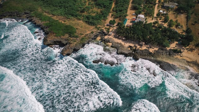 Stunning aerial photo showcasing Bolinao's rugged coastline with crashing waves and lush greenery.