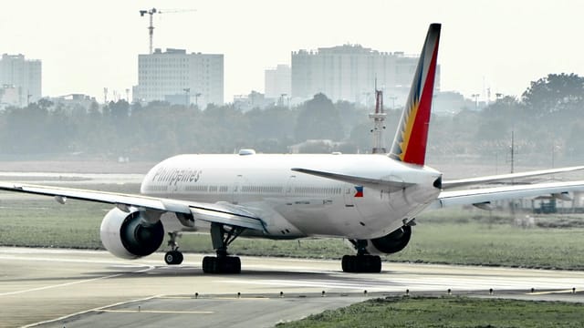 Airplane taxiing at an airport runway with city skyline in the background.