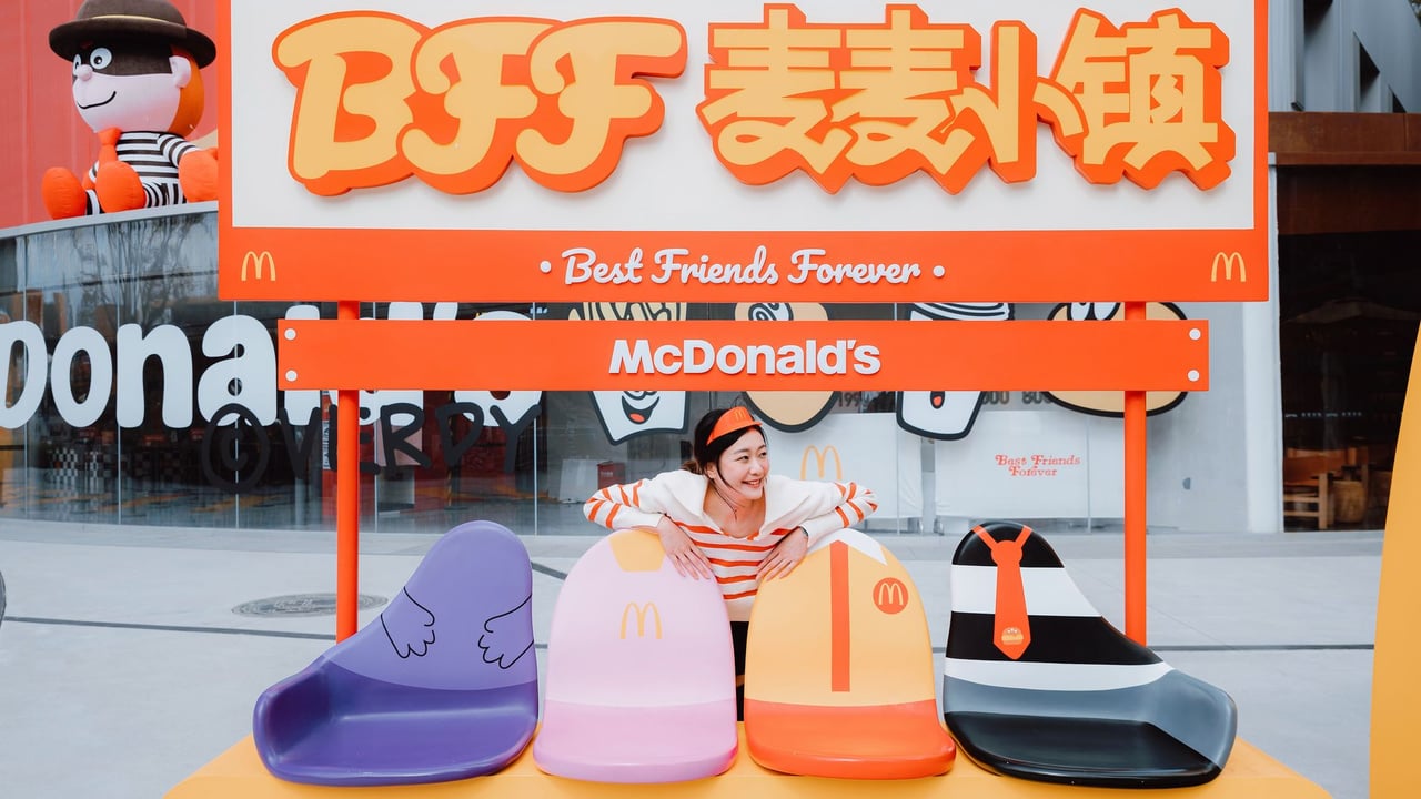 Asian woman smiling at colorful McDonald's BFF seating area outdoors.