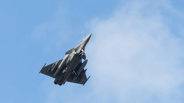 A sleek military jet fighter captured ascending against a bright blue sky.
