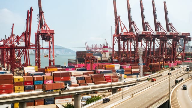 A vibrant view of Hong Kong's bustling shipping port with red cranes and stacked containers.