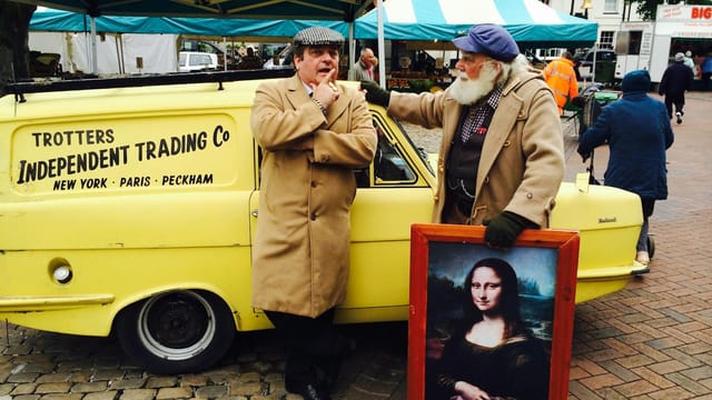 Two men in vintage attire at Aylesbury Market with a classic yellow car and Mona Lisa painting.