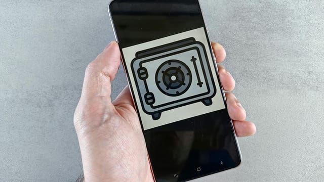 Close-up of a smartphone showing a safe icon held in a hand, symbolizing digital security.
