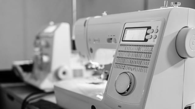 A detailed black and white close-up of a modern sewing machine showcasing its digital controls and patterns.