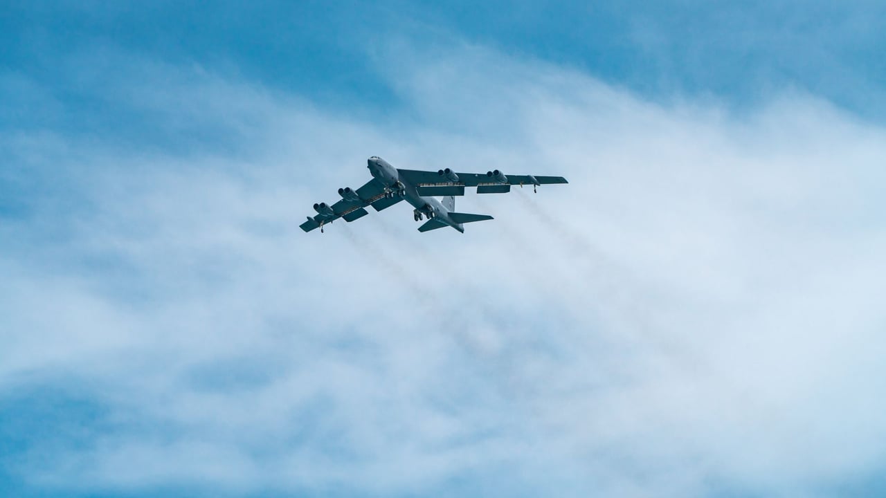 A B-52 Stratofortress aircraft soars through a clear blue sky on a sunny day.