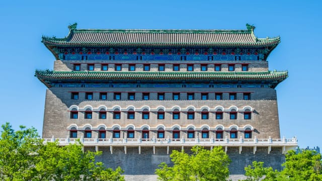 View of the iconic Zhengyangmen Gate Tower under a clear blue sky with vibrant green trees.
