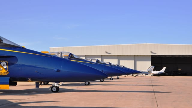 Blue fighter jets aligned on the tarmac in front of an aircraft hangar on a clear day.