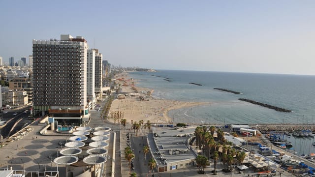 Aerial view of Tel Aviv's beachfront, skyscrapers, and marina on a clear day.