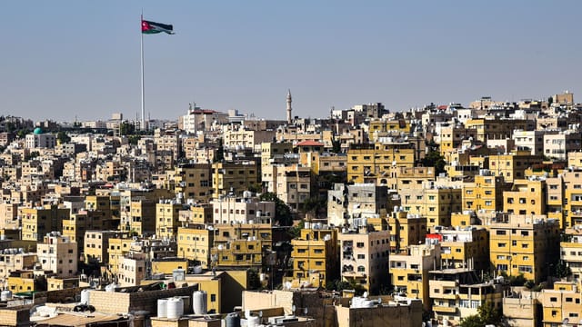 A panoramic view of Amman's densely packed buildings and a prominently flying flag.
