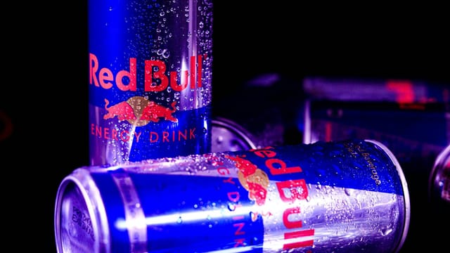 Close-up of chilled Red Bull cans with water droplets, reflecting vibrant neon lighting.