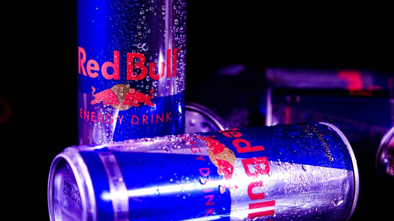Close-up of chilled Red Bull cans with water droplets, reflecting vibrant neon lighting.