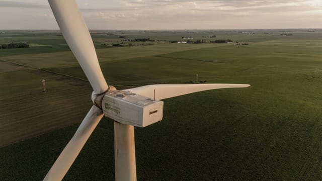 Aerial shot of a wind turbine amidst vast agricultural fields during sunset, highlighting renewable energy and farming.