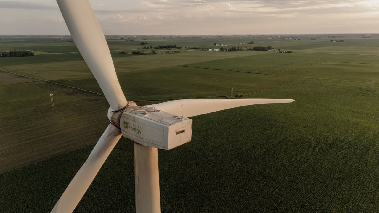 Aerial shot of a wind turbine amidst vast agricultural fields during sunset, highlighting renewable energy and farming.