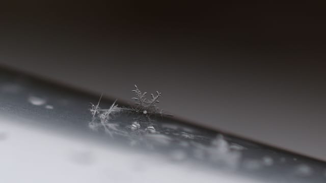 Macro shot of a delicate snowflake resting on a reflective surface, highlighting its intricate patterns.