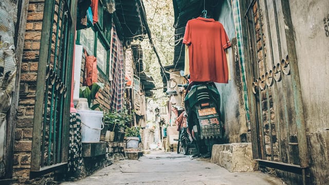 A rustic alleyway in Beijing, China, with clothes hanging and a parked motorcycle, depicting daily life.
