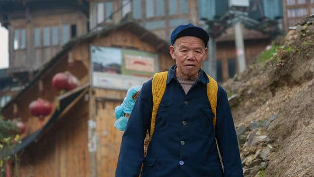An elderly man in traditional clothing walks through a historic village in Guilin, China.