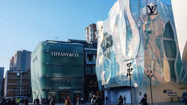 Outdoor view of Tiffany & Co and Louis Vuitton stores in a bustling city plaza.