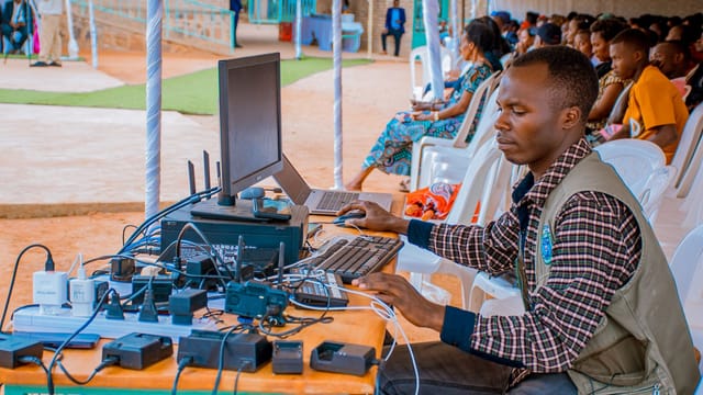 Technician managing electrical and computer setup at an outdoor event with attentive audience.