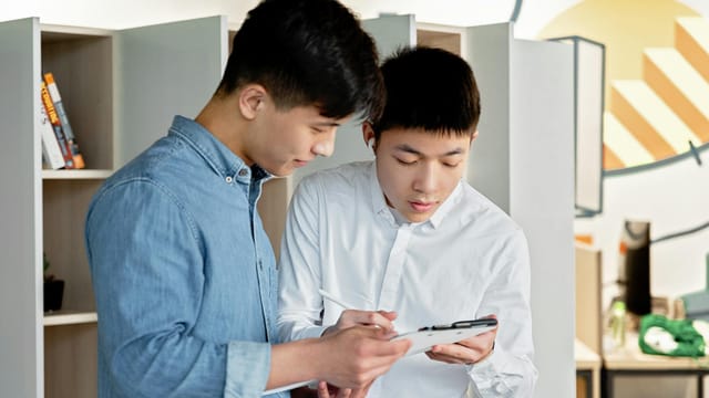Two young men collaborating on a project using a digital tablet in a modern office environment.