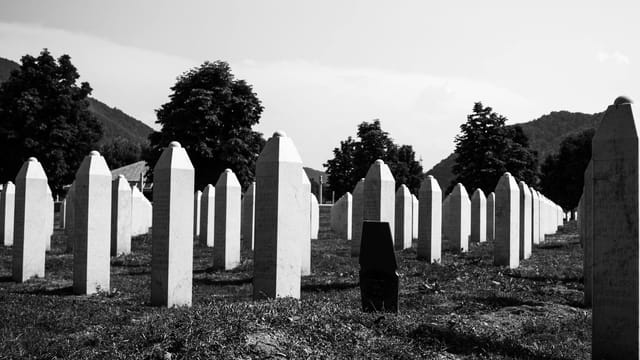 Black and white photo of the Srebrenica Genocide Memorial Cemetery in Bosnia, showcasing rows of grave markers.