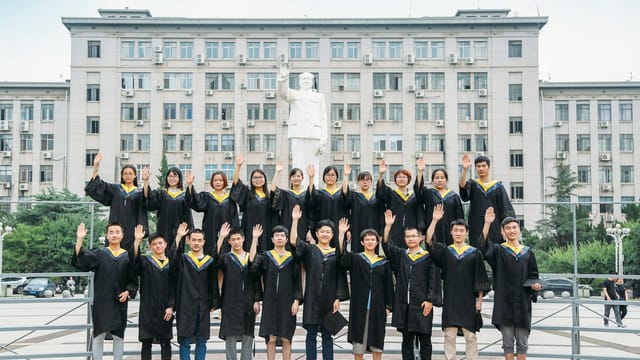 Group of graduates in gowns posing outdoors in front of university building.