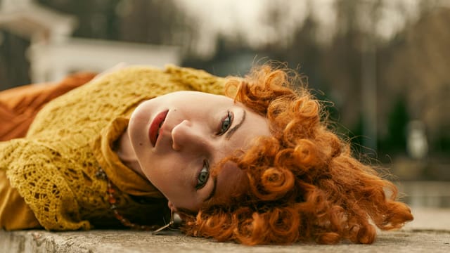 Artistic portrait of a woman with red curly hair lying on a stone surface in Lviv Oblast, Ukraine.