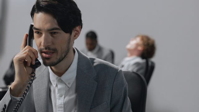 Young businessman in gray suit on phone, emphasizing office communication.