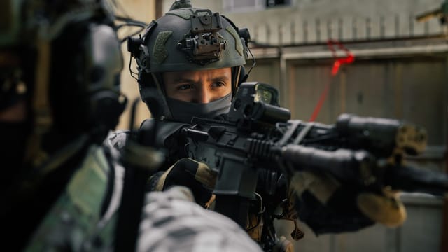 Focused soldier in tactical gear aiming rifle during an outdoor operation.