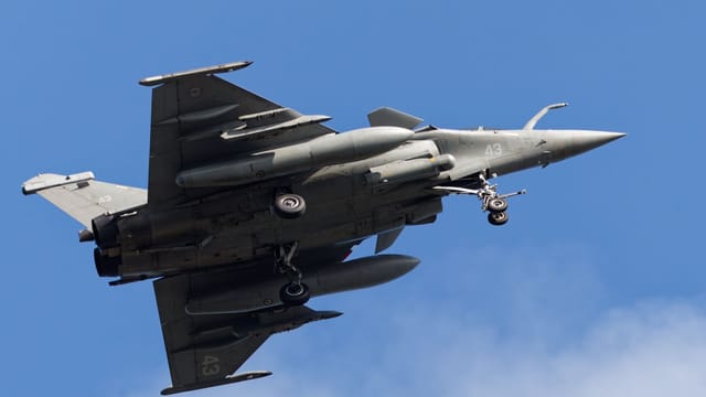 French Rafale fighter jet flying over Bretagne, France with landing gear deployed.