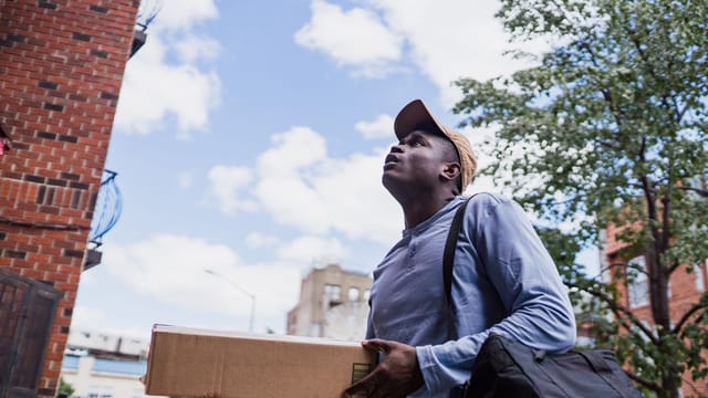 Illustrative image: Man delivering a package in a city neighborhood, looking up at the building.