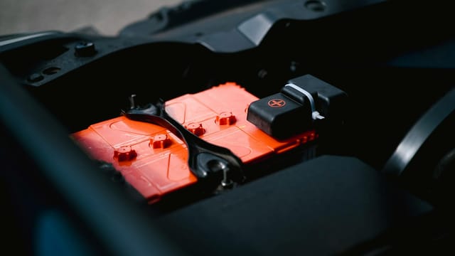 Detailed view of an orange car battery inside a vehicle's engine bay, highlighting its features.