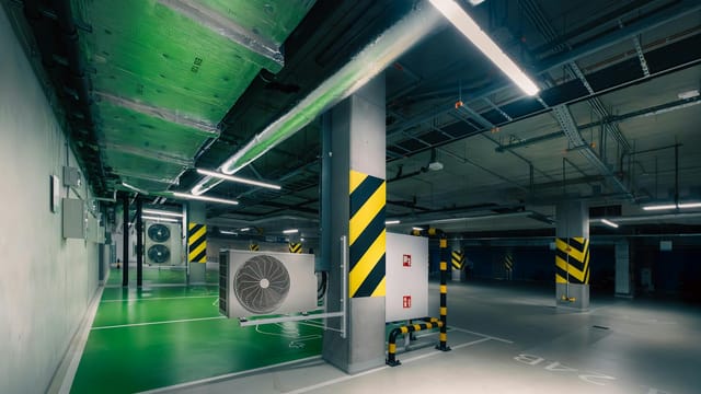 Sleek underground parking area with air conditioning units and green lighting.