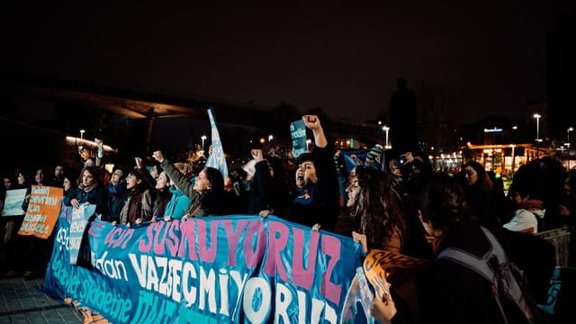 A group of protesters holding banners during a nighttime protest in İstanbul, Türkiye.