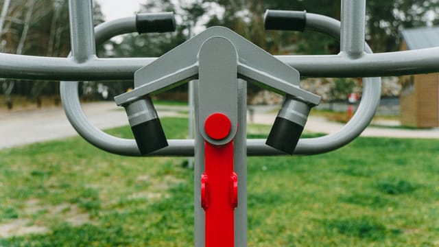 Outdoor exercise equipment with focus on red detail, set in a lush Polish park during spring.