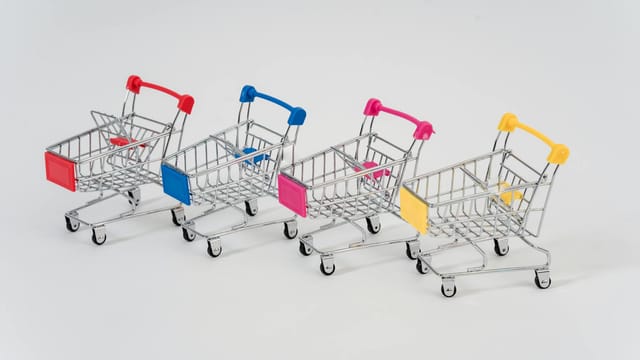 Four miniature shopping carts with colorful handles aligned on a white background for conceptual business imagery.