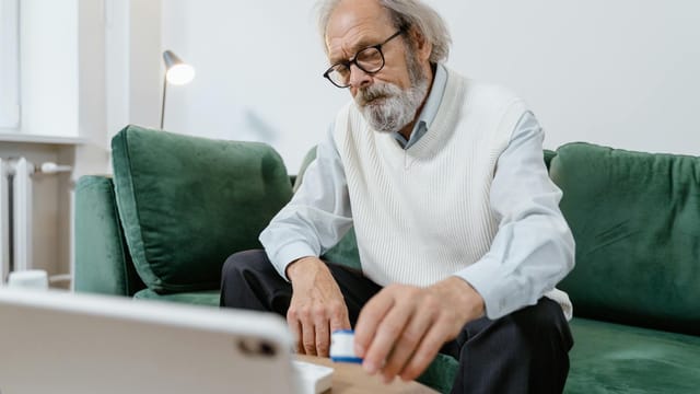 Elderly man with glasses using a tablet for telehealth consultation at home.