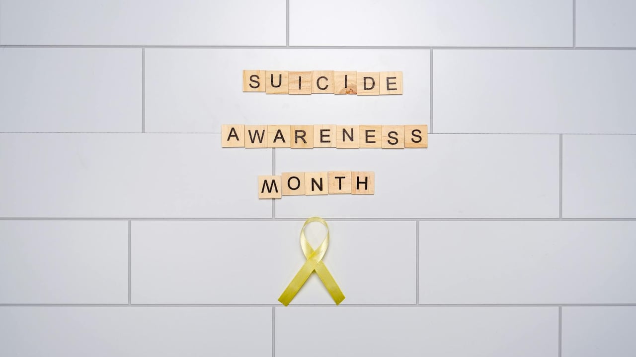 Scrabble tiles and yellow ribbon promoting Suicide Awareness Month on a tile background.