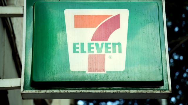 A close-up of a 7-Eleven store sign in a city environment, outdoors.