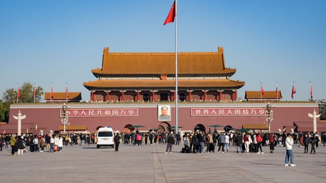 Crowds gather at the iconic Forbidden City Gate in Tiananmen Square, Beijing, under a clear sky.