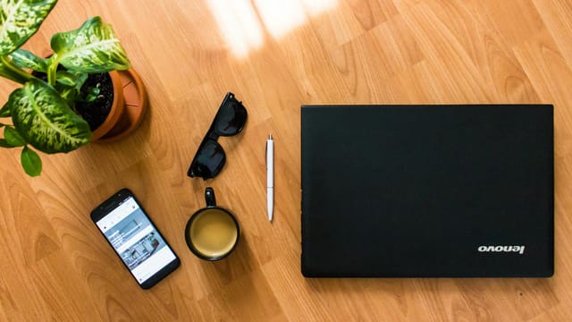 A flat lay of a desk with a laptop, coffee cup, smartphone, and plant, perfect for a modern office setting.