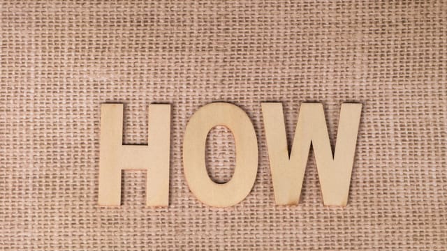 Word 'HOW' formed with wooden letters on textured burlap surface.