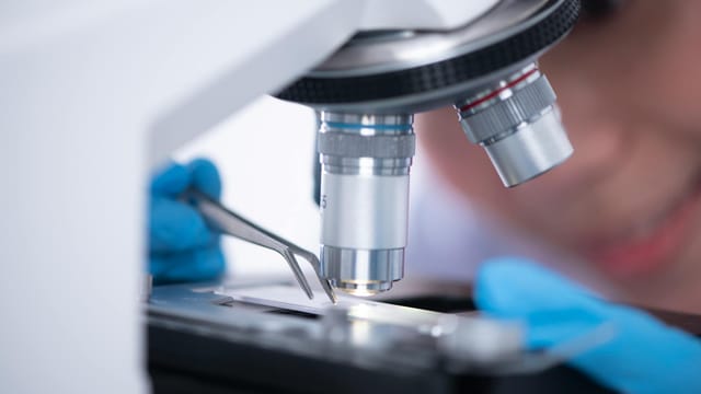 Blurred unrecognizable person placing sample on microscope while making research during work in modern laboratory