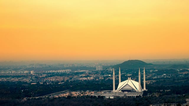Captured from above, Islamabad's Faisal Mosque silhouetted against a vibrant sunset sky.