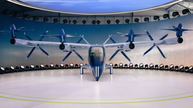 Front view of a futuristic electric vehicle with propellers displayed indoors.
