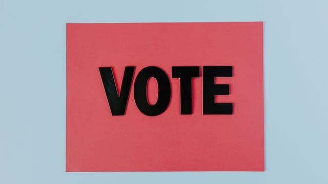 Black letters spelling 'VOTE' on red paper, emphasizing political participation.