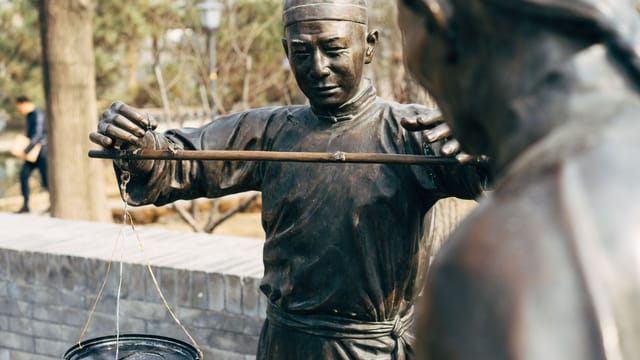 Bronze statues depicting traditional Chinese weighing scales at an outdoor market.
