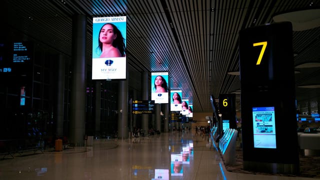 Empty airport hallway with digital displays and glossy floors at night.