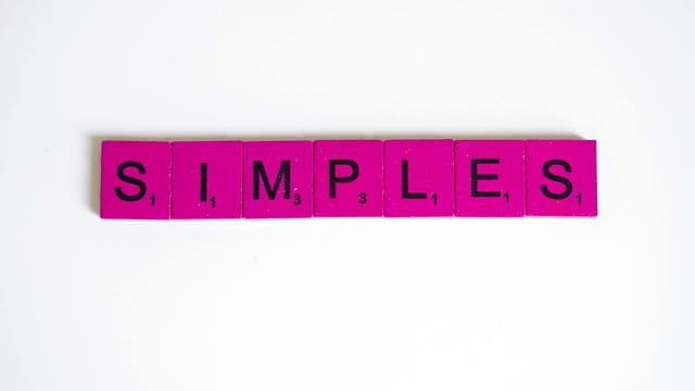 Pink Scrabble tiles forming the word 'SIMPLES' on a white surface.