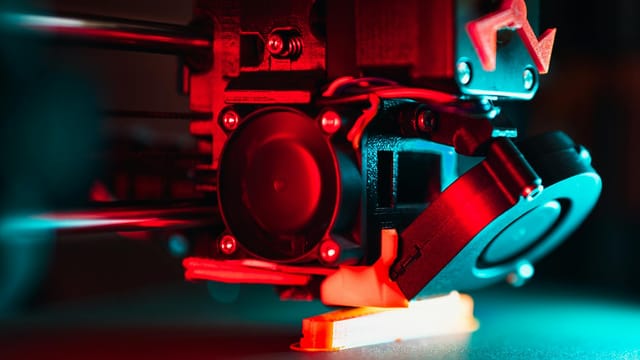 Vibrant close-up of a 3D printer creating a prototype with red and blue lights.