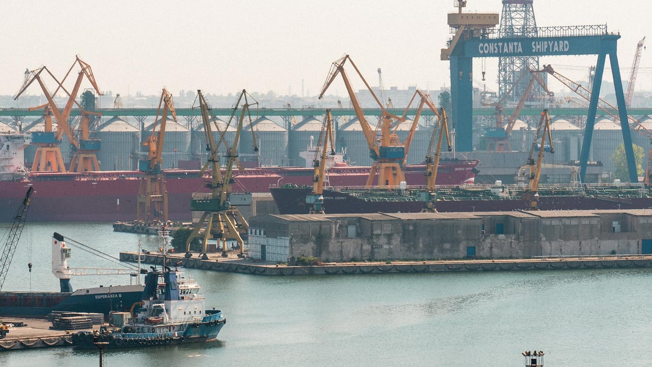 A busy scene at Constanta Shipyard, Romania, featuring cranes and cargo ships in the harbor.